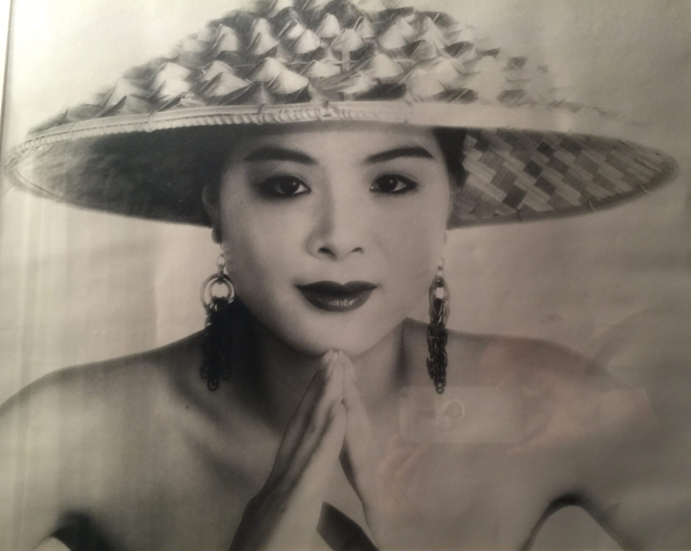 Beautiful young Chinese girl wearing only triangle straw hat with hair tucked up into it looking directly at you with long hanging tassel earrings and hands placed together in triangle prayers fashion